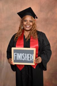 Sheryl, May's featured Diva in her cap and gown holding a "Finished" sign