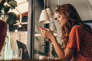 woman wearing red polka dot shirt at cafe on smartphone