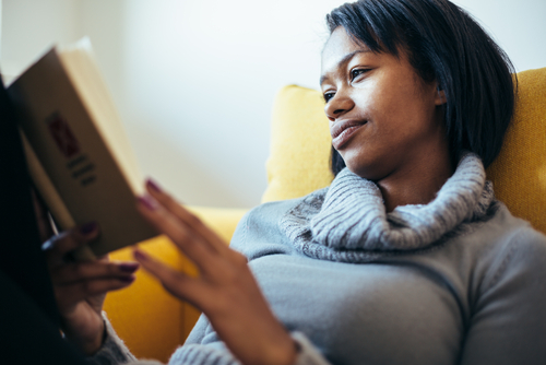 African American woman reading a book peacefully on couch