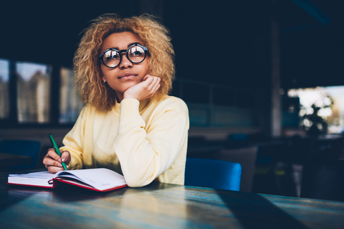 young african american woman with glasses looking thoughtfully with a book